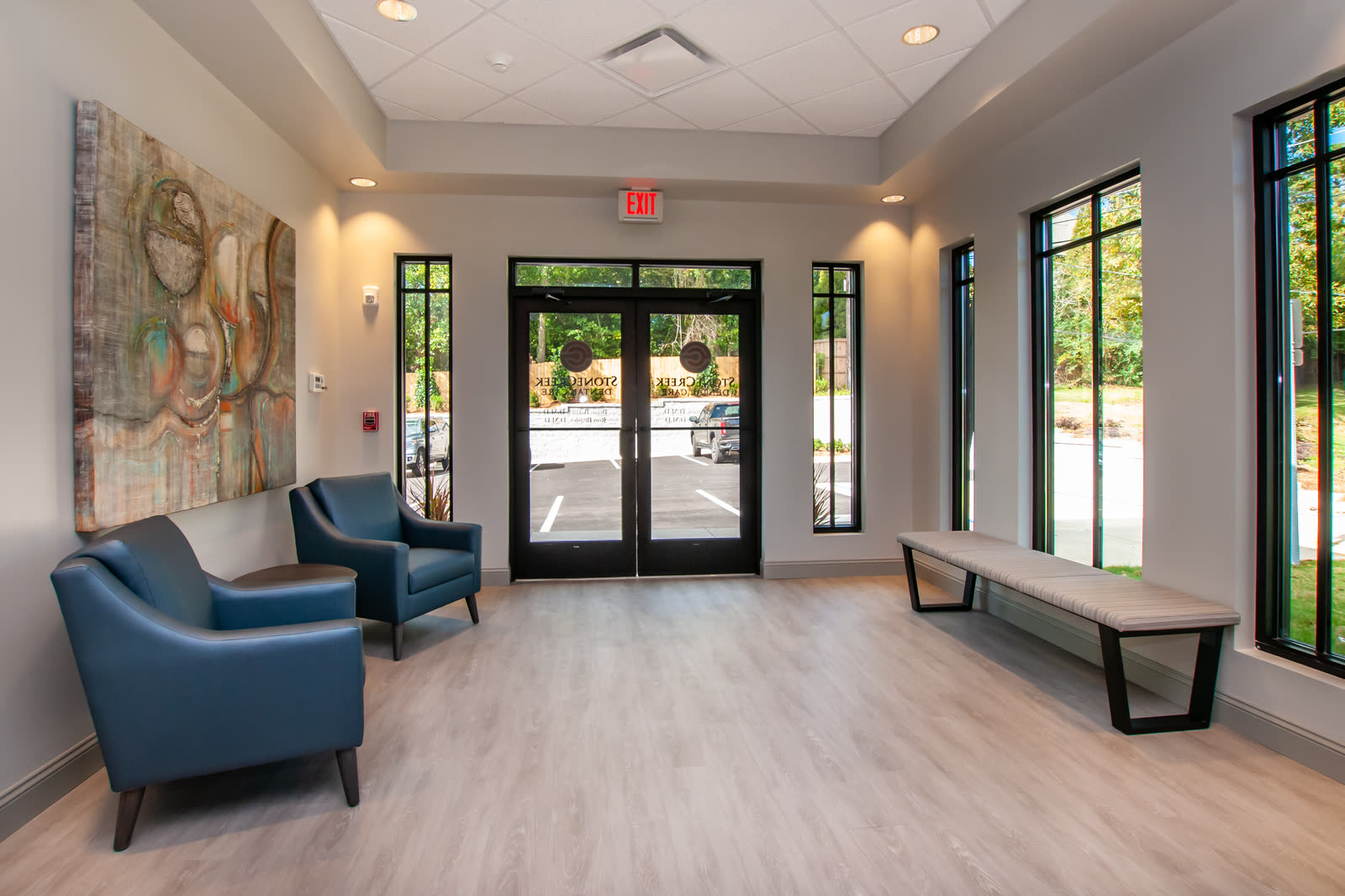 Entrance lobby with armchairs, a bench and glass doors onto the car park